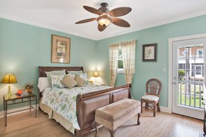 A bedroom with a bed, a chair, a bench, a nightstand, a lamp, and a ceiling fan. - Purple Parrot Condo Near Beach with Pool (Pensacola)