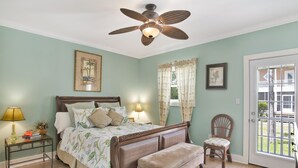 Une chambre à coucher comprenant un lit, une chaise, un banc, une table de chevet, une lampe et un ventilateur de plafond.