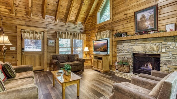 A cozy log cabin interior with a stone fireplace, wooden walls, and a comfortable seating area.