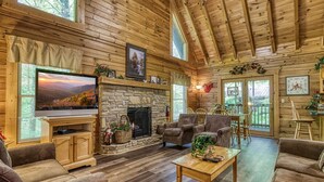 A cozy cabin interior with a stone fireplace, wooden walls, a television, and comfortable seating.