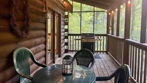 A wooden cabin with a covered porch, a grill, and a table with chairs.