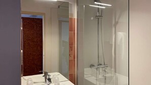 A modern bathroom with a glass shower enclosure, a white sink, and a mirror.