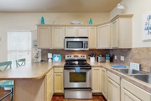 A kitchen with a microwave, stove, and sink, light-colored cabinets, and a welcome sign.
