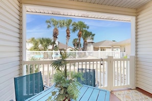 A covered outdoor area with a table and chairs, a railing, and palm trees in the background.