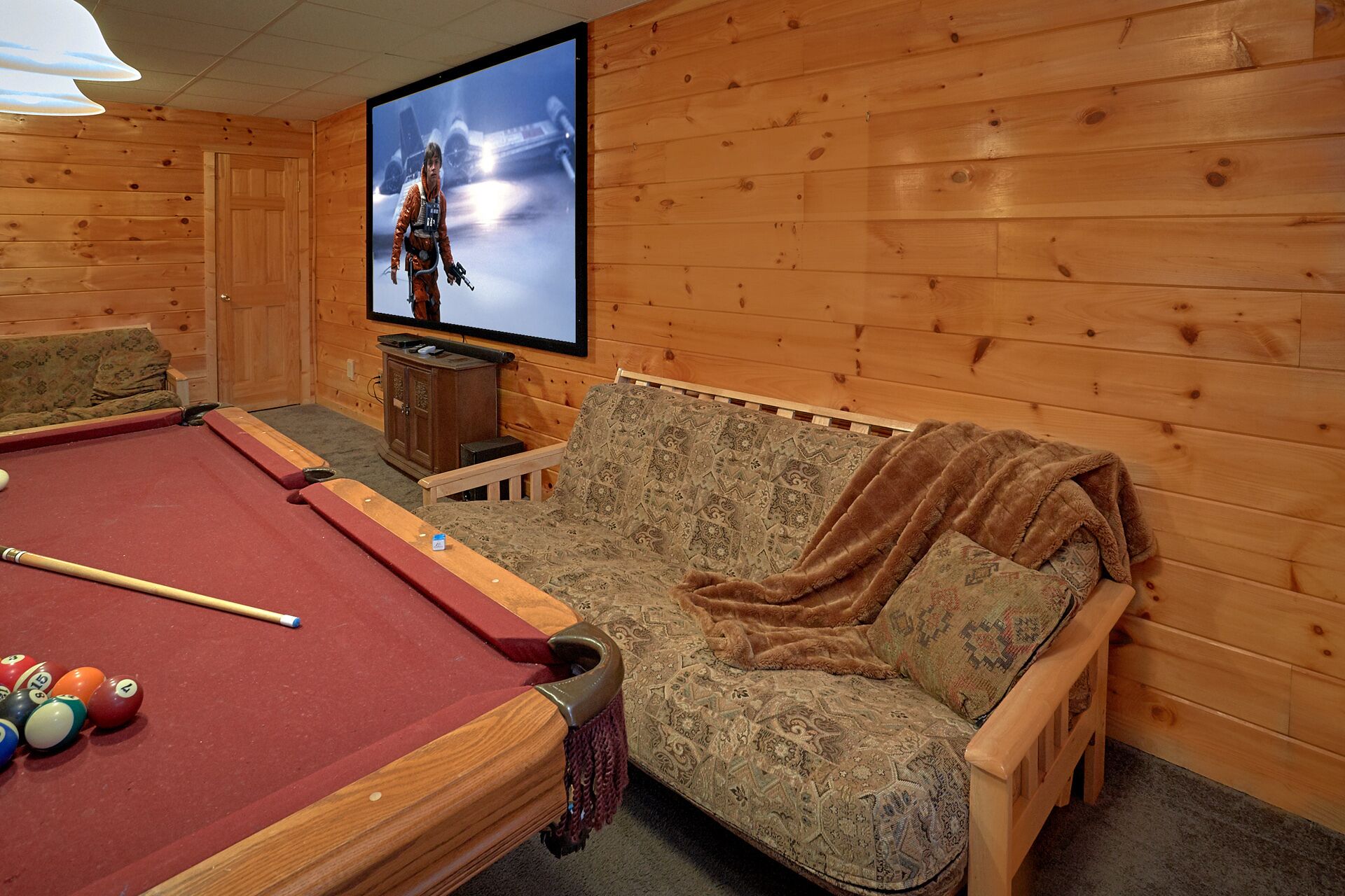 A cozy room with a pool table, a sofa, and a television displaying a movie scene.