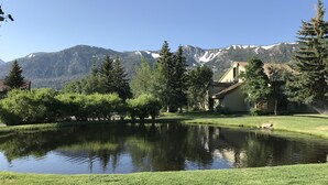 A serene lakeside scene with a house, trees, and mountains in the background.