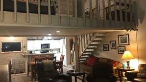 A loft-style living area with a staircase, a kitchen in the background, and a cozy seating arrangement.