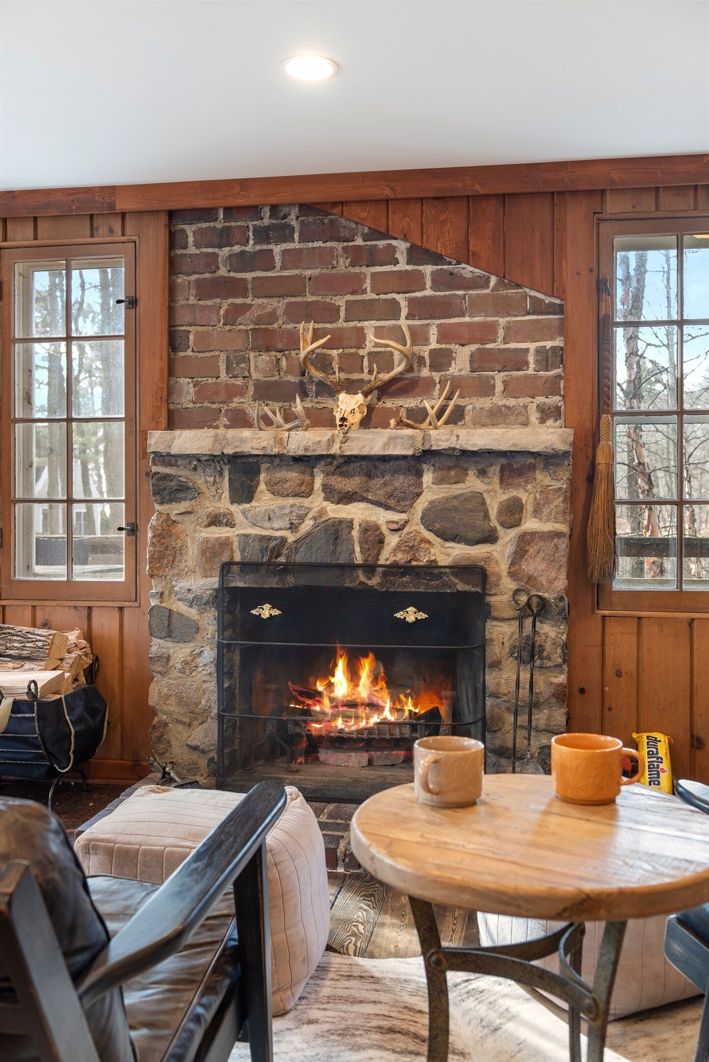 A cozy room with a stone fireplace, wooden walls, and a round table with two mugs.