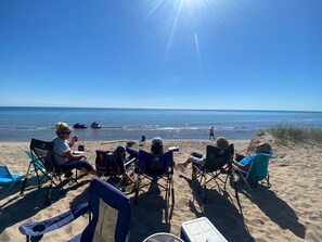 Een strand met mensen die in klapstoelen zitten en naar de oceaan kijken, een heldere lucht en een rustige zee.