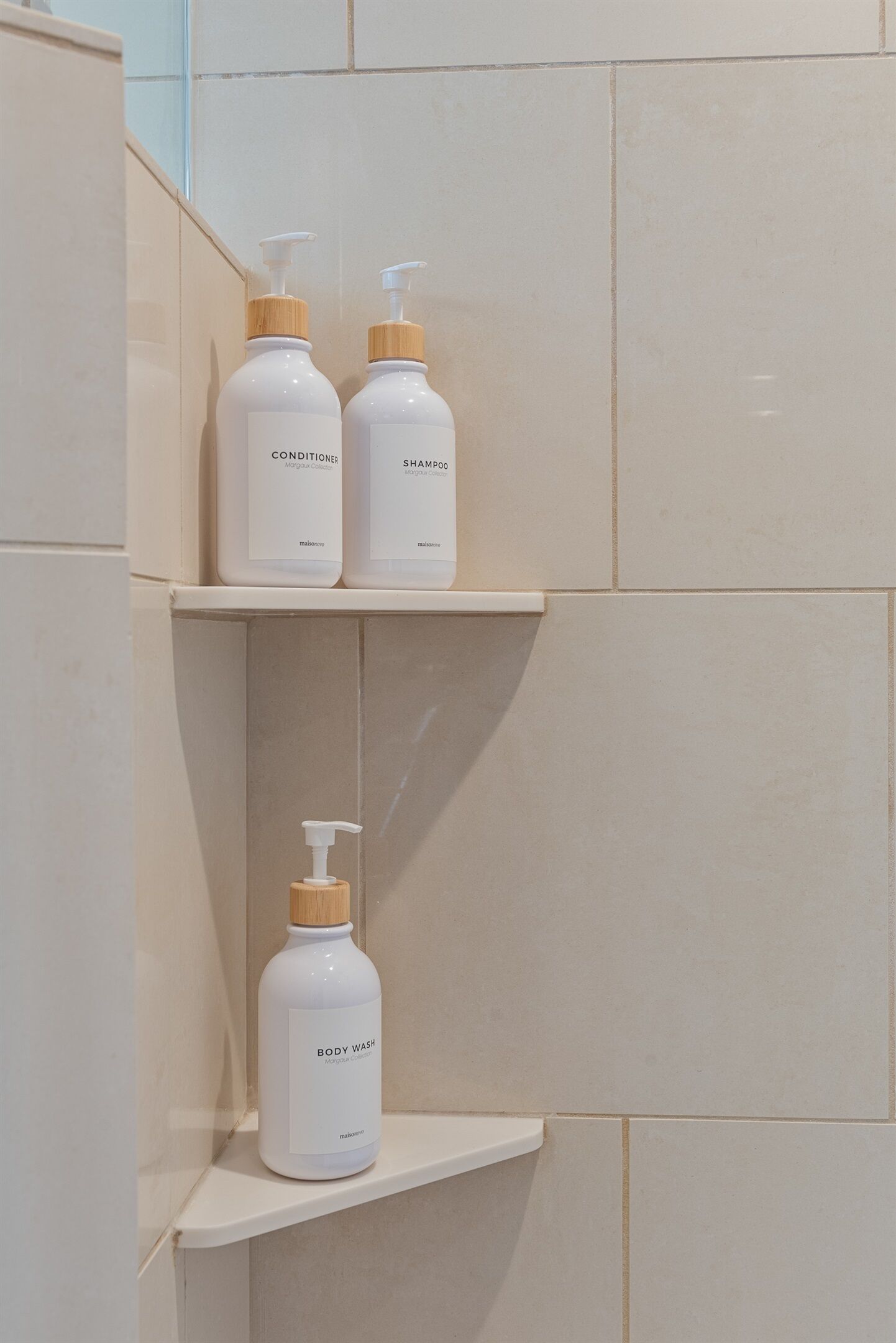 A bathroom shelf with three white bottles labeled 'CONDITIONER,' 'SHAMPOO,' and 'BODY WASH.'