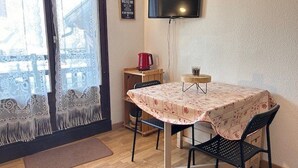 Et lille værelse med et bord og stole, et fjernsyn ophængt på væggen, og et vindue med udsigt til en bygning.
