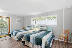 A bedroom with two beds, a window with curtains, a chair, and a small table.