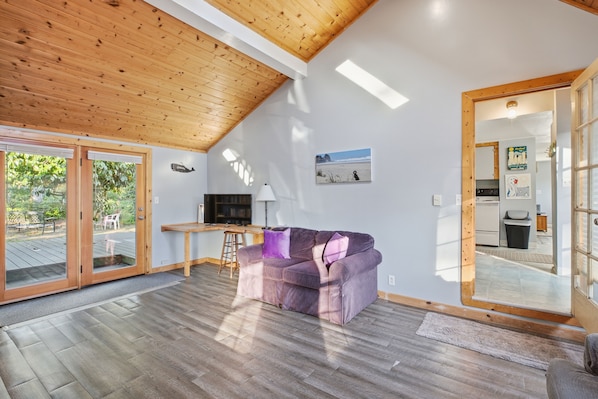 A modern living room with a wooden ceiling, a purple sofa, a TV, and a sliding glass door leading to an outdoor area.