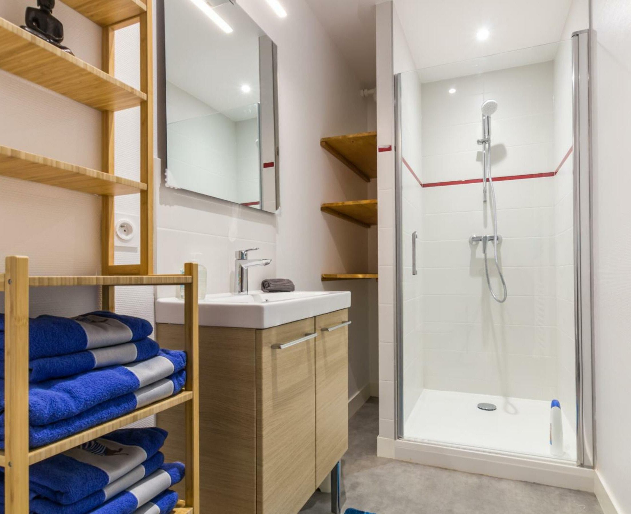 Ein modernes Badezimmer mit einer Duschkabine aus Glas, Holzböden mit Handtüchern und einem weißen Waschbecken.