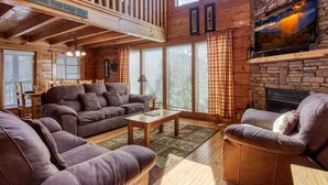L’intérieur chaleureux d’un chalet avec une terrasse en bois, une cheminée et une grande fenêtre donnant sur un paysage magnifique.
