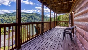 Une terrasse en bois avec un banc, offrant une vue sur une zone montagneuse boisée.