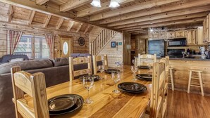 L’intérieur chaleureux d’un chalet comprend une table à manger en bois pour quatre personnes, un canapé et un coin cuisine équipé d’appareils électroménagers modernes.