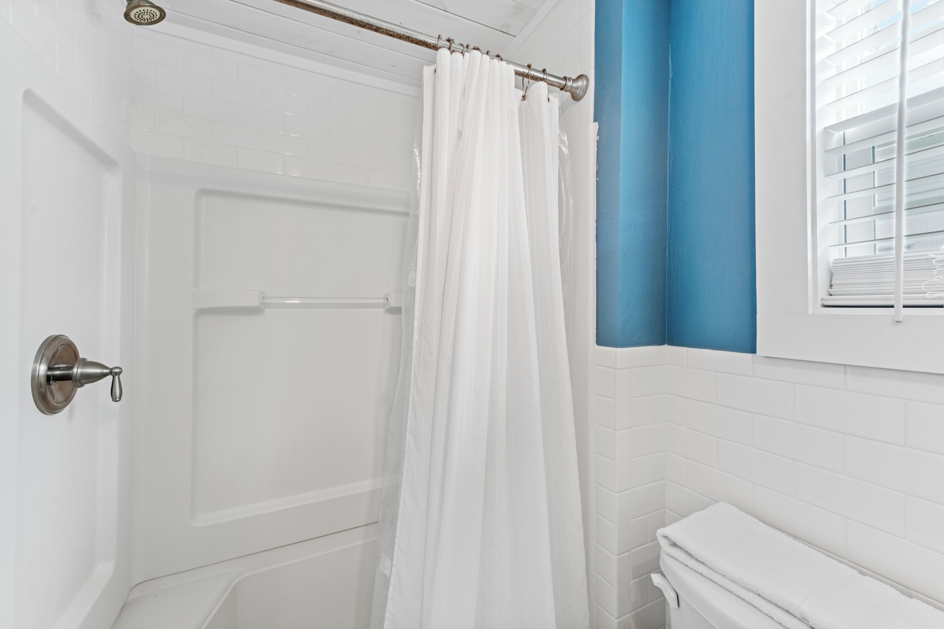 A bathroom with a white shower curtain, a white toilet, and a window with blinds.