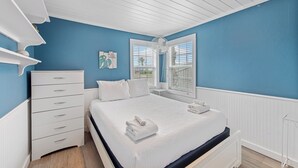 Une chambre à coucher avec un lit, une commode blanche et une fenêtre avec des stores.