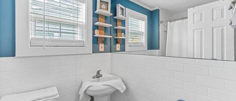 Un baño con azulejos blancos, un lavabo, un perchero para toallas y una ventana con persianas.