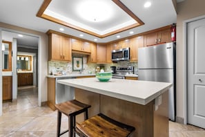 Une cuisine moderne avec des meubles en bois, un îlot central, un four à micro-ondes, un réfrigérateur et un extincteur.