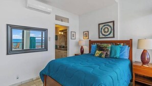 A bedroom with a large bed, a window with a view, a ceiling fan, and a framed picture on the wall.