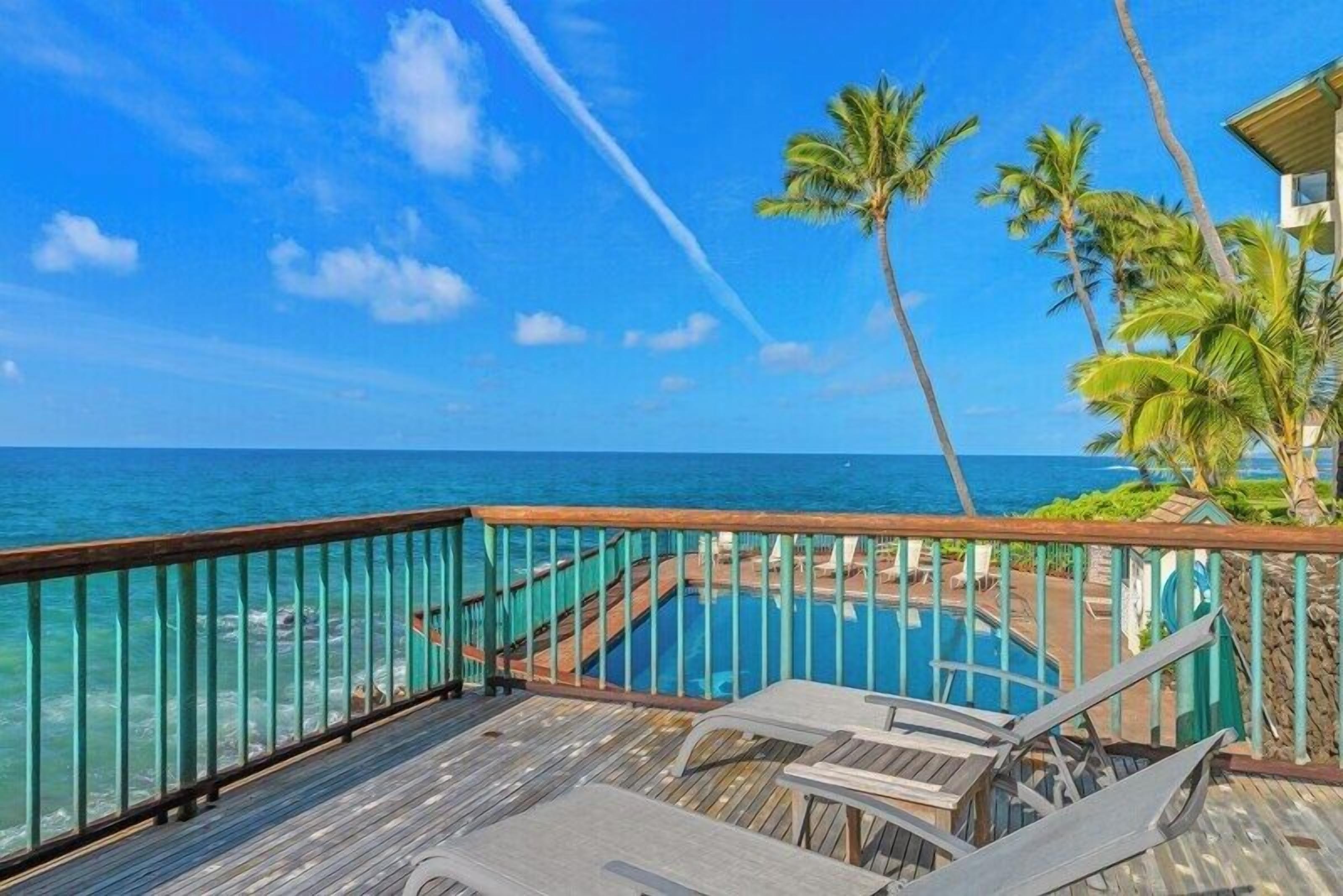 A wooden deck with lounge chairs overlooking a pool and the ocean.