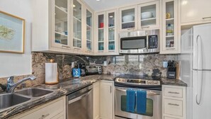 A modern kitchen with stainless steel appliances, marble countertops, and light-colored cabinetry.