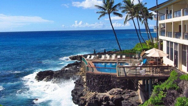 A resort with a pool overlooking the ocean, palm trees, and a building with balconies.