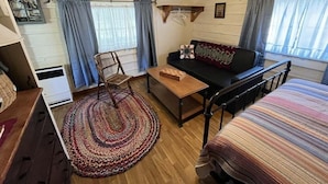 A cozy room with a bed, a sofa, a chair, a small table, and a window with curtains.