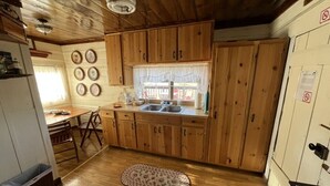 A kitchen with wooden cabinets, a window with a curtain, a sink, and a dining table with chairs.