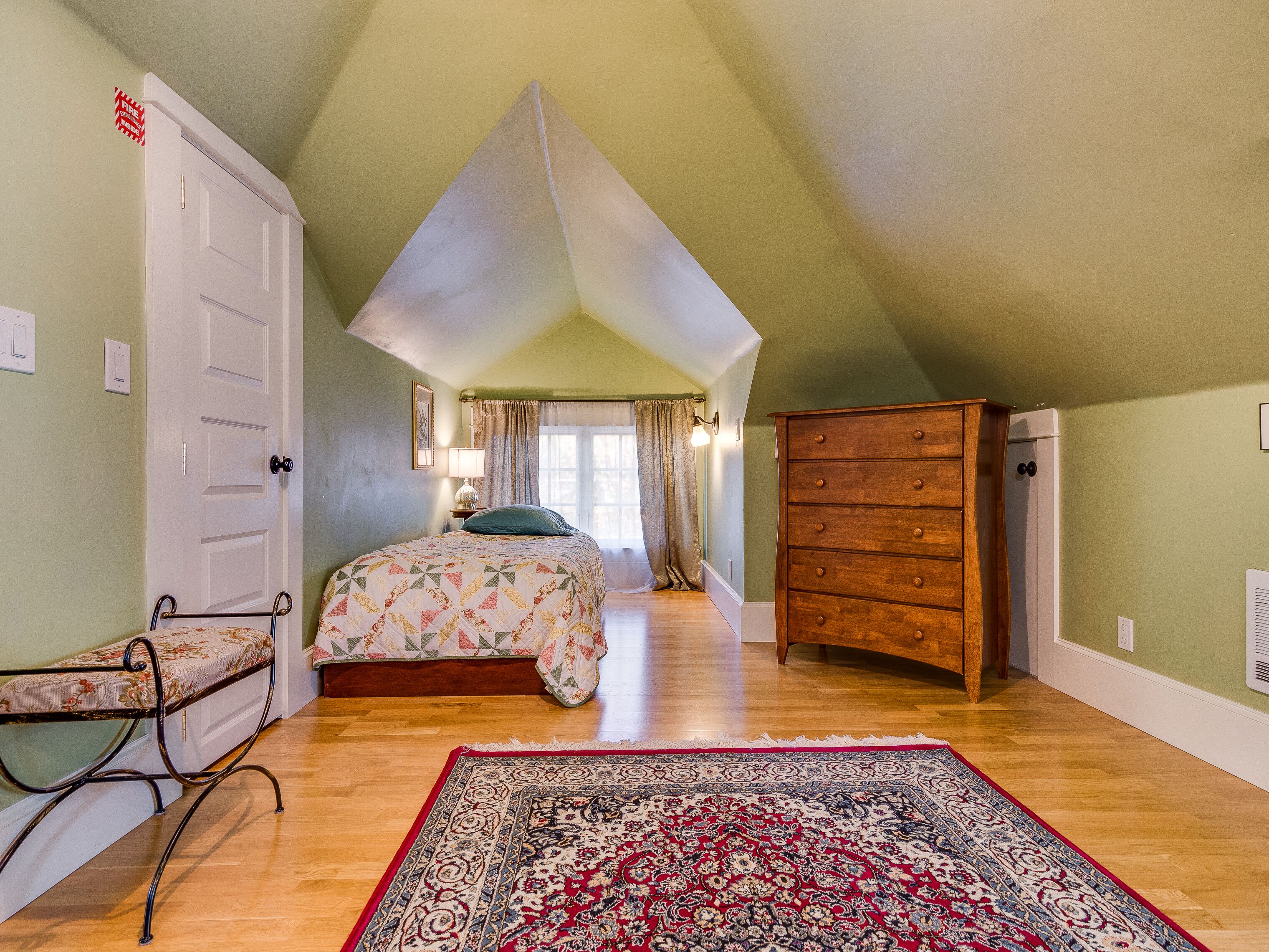 A bedroom with a bed, a dresser, a bench, and a rug.