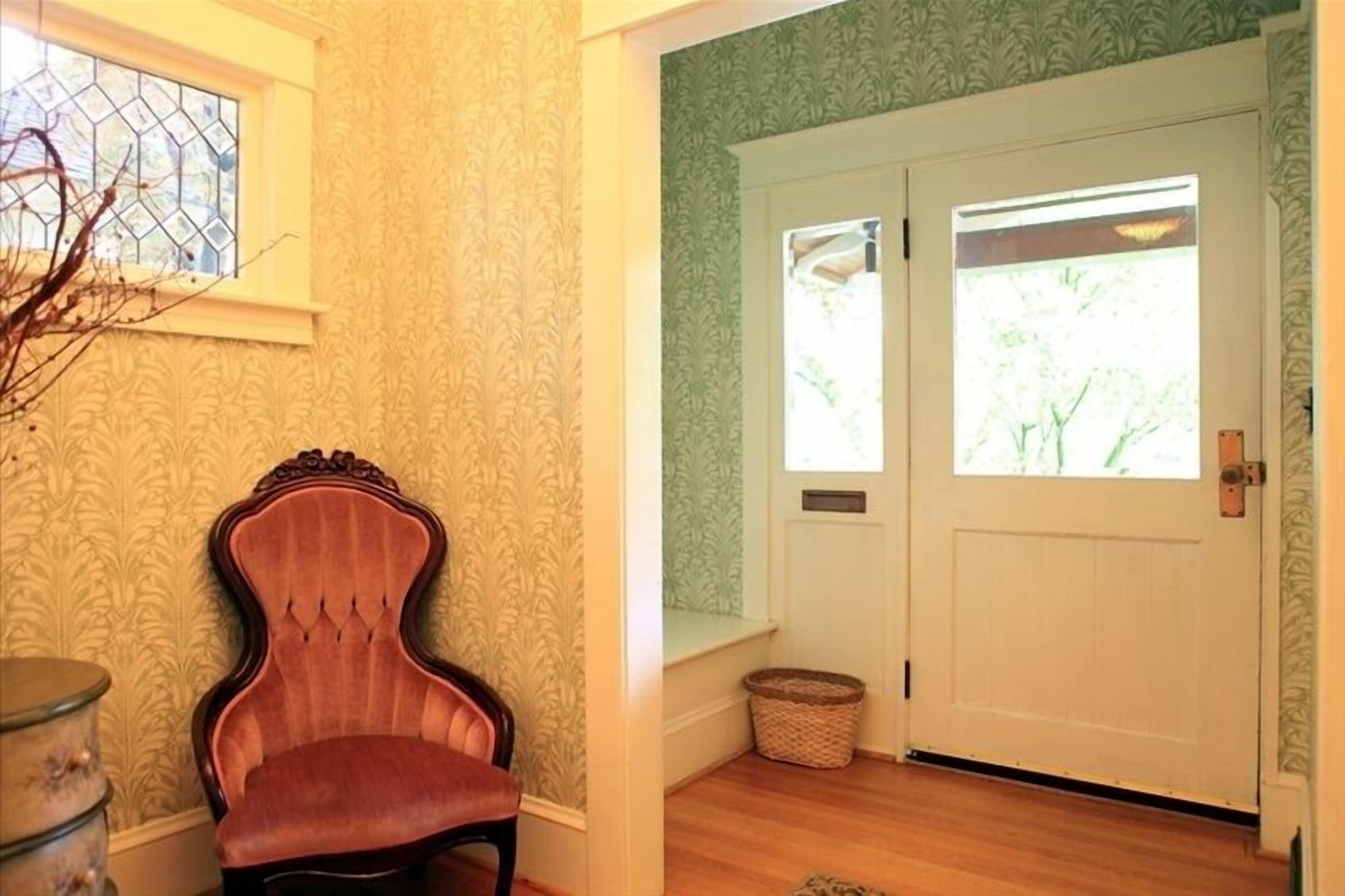 Une pièce avec un papier peint à motifs, une chaise en bois, une porte blanche avec des fenêtres et un petit panier.