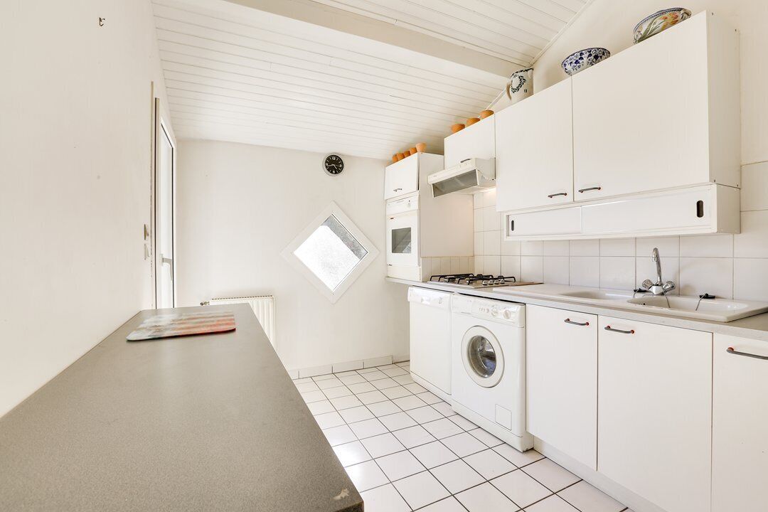 A compact kitchen with white cabinets, a washing machine, a stove, and a sink.