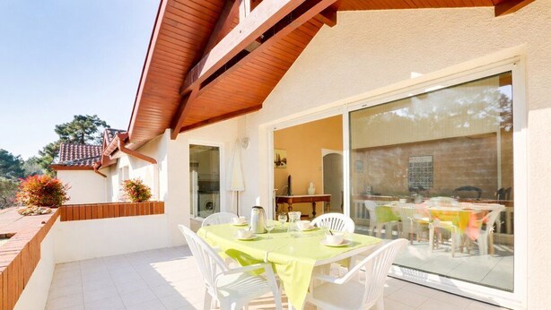 Un patio con mesa lista para comer, sillas blancas y techo de madera.