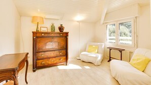 Una habitación con un aparador de madera, un sofá blanco, una mesita y una ventana con vistas a zonas verdes.