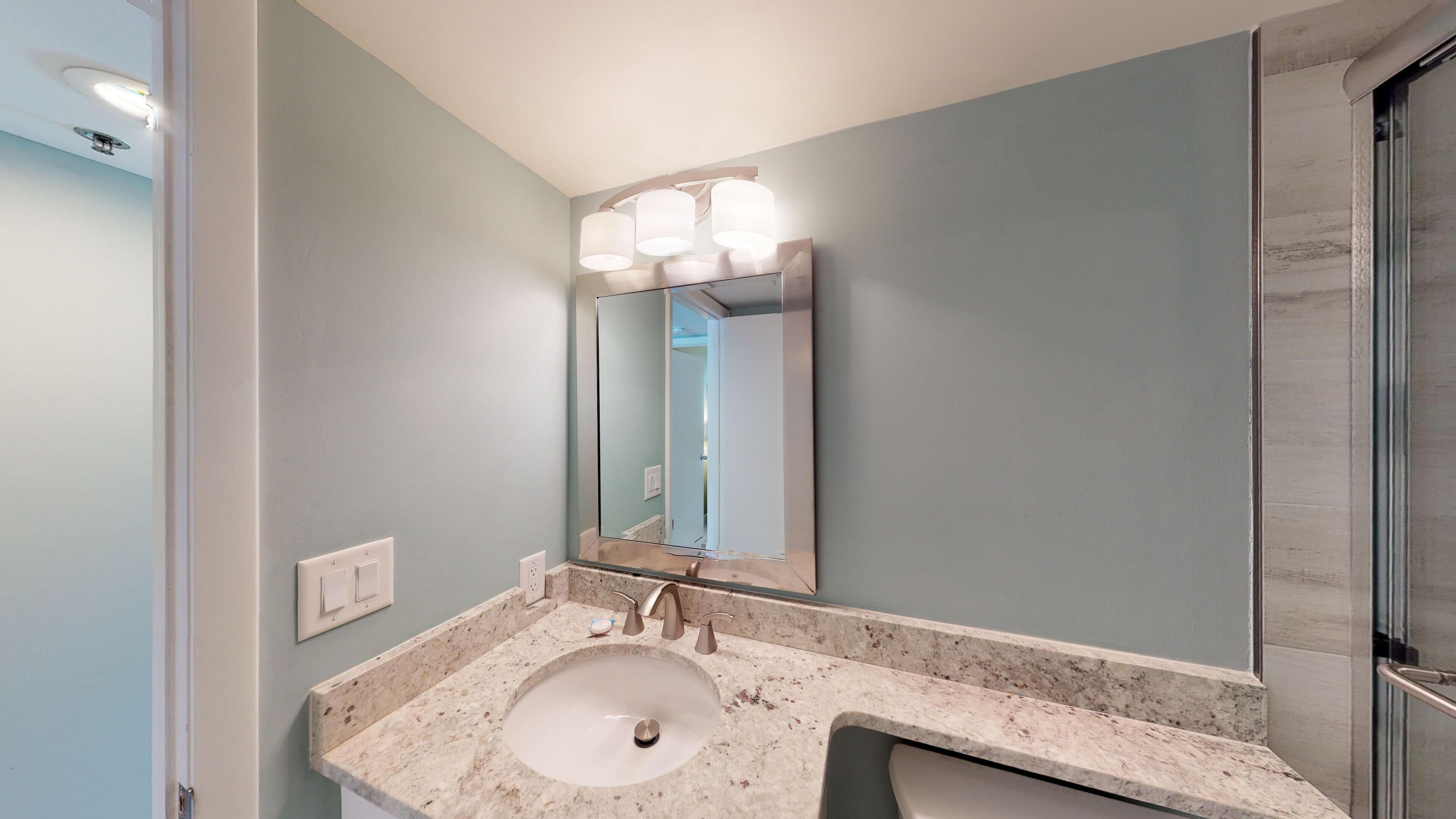 Une salle de bain avec un lavabo en marbre, un grand miroir et un luminaire placé au-dessus du miroir.