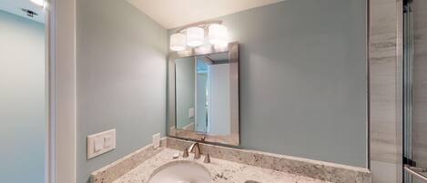 Une salle de bain avec un lavabo en marbre, un grand miroir et un luminaire placé au-dessus du miroir.