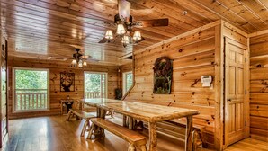 A wooden cabin interior with a large dining table, benches, a ceiling fan, and large windows. - Big Bear Lodge: Mountain Views, Game Room (Sevierville)