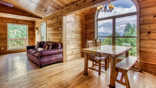 A wooden cabin interior with a wooden ceiling, a dining table with benches, a purple leather sofa, and large windows offering a view of the outdoors. - Big Bear Lodge: Mountain Views, Game Room (Sevierville)