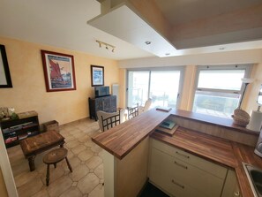 A modern kitchen with a wooden countertop, a dining area with hexagonal tiles, and a balcony with a view.