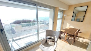 A balcony with a glass door, a dining table with chairs, and a view of the sea. - 2-Bedroom Apartment Sea View - Parking, Pets Allowed (Les Sables-d'Olonne)