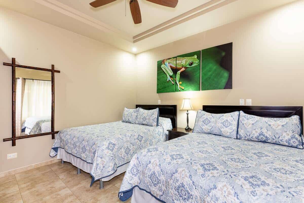 A hotel room with two beds, a ceiling fan, a large mirror, and a wall-mounted artwork of a frog.