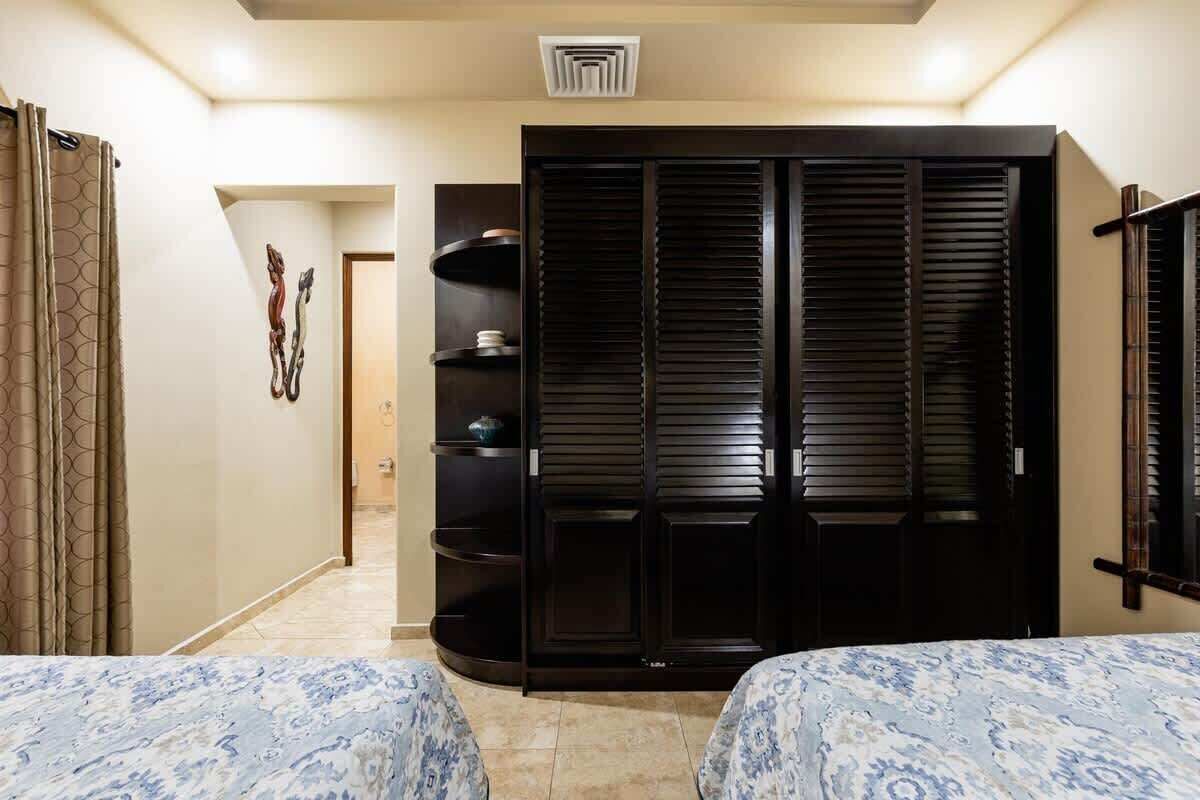 A bedroom with two beds, a wardrobe, and a bathroom visible through an open door.