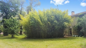 A grassy area with trees and a building with a stone facade. - Homerez - Villa in Crastes with pool (Crastes)