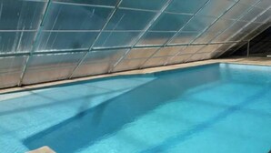 An indoor swimming pool with a glass ceiling, clear blue water, and a small poolside area with a lifeguard chair.