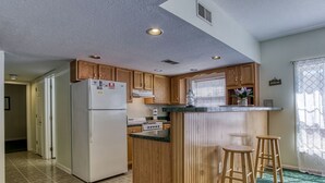 Une cuisine compacte avec des meubles en bois, un réfrigérateur blanc, une cuisinière encastrée et un petit coin bar avec des tabourets.