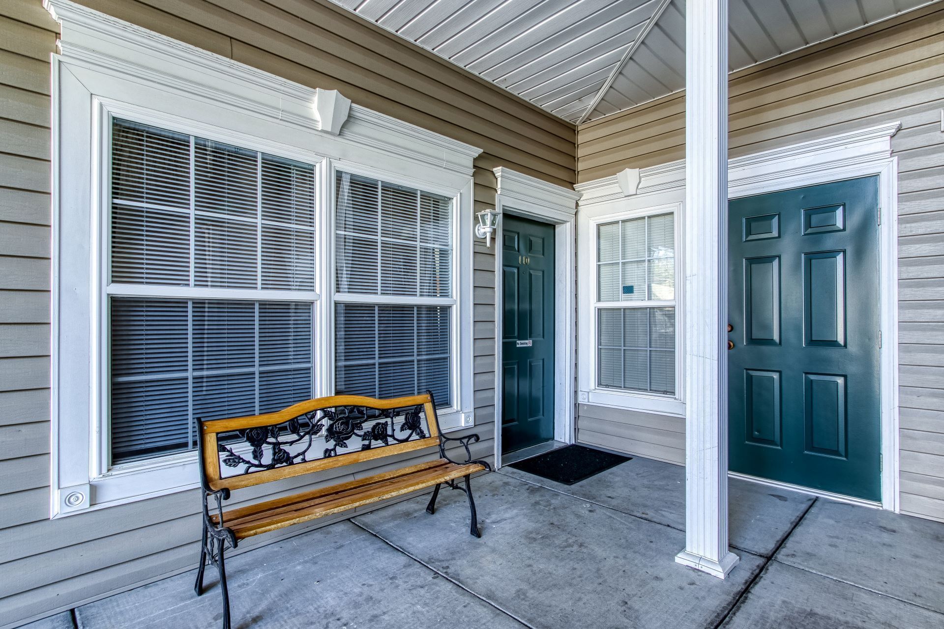 A porch with a bench, a green door, and large windows with blinds.