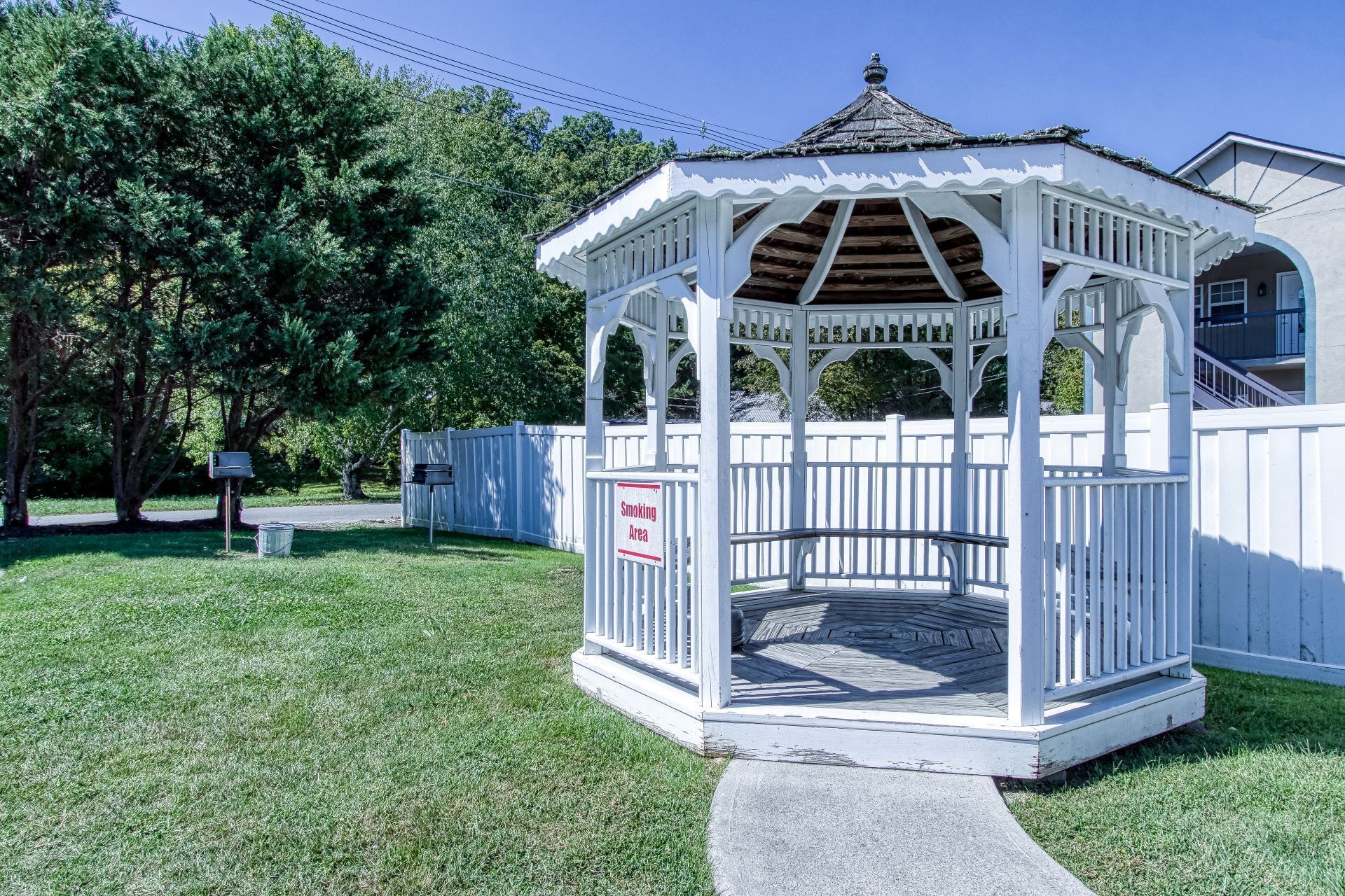 A gazebo with a white exterior and a wooden roof, surrounded by a white fence.