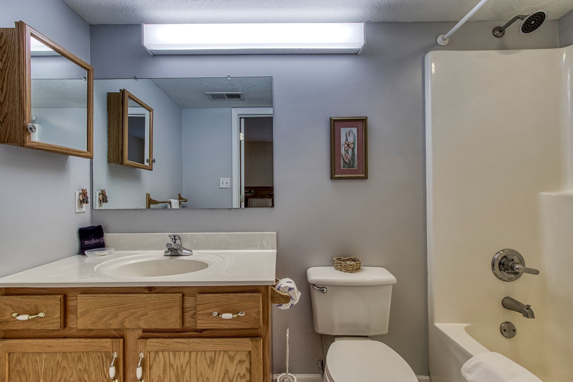 A bathroom with a wooden vanity, a large mirror, a toilet, and a shower.